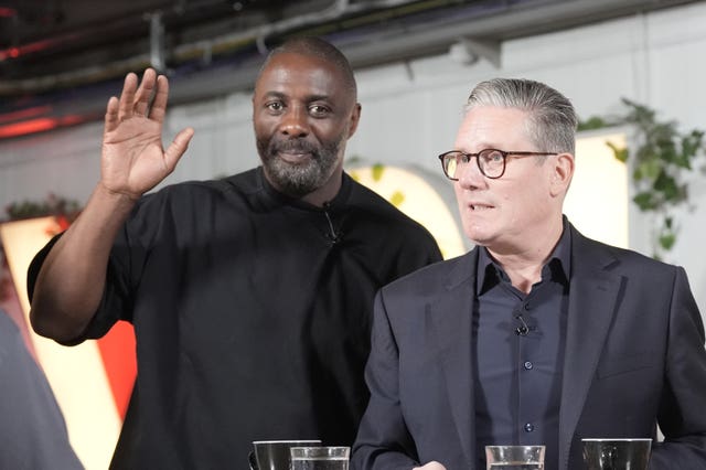 Idris Elba, hand raised, standing alongside Sir Keir Starmer